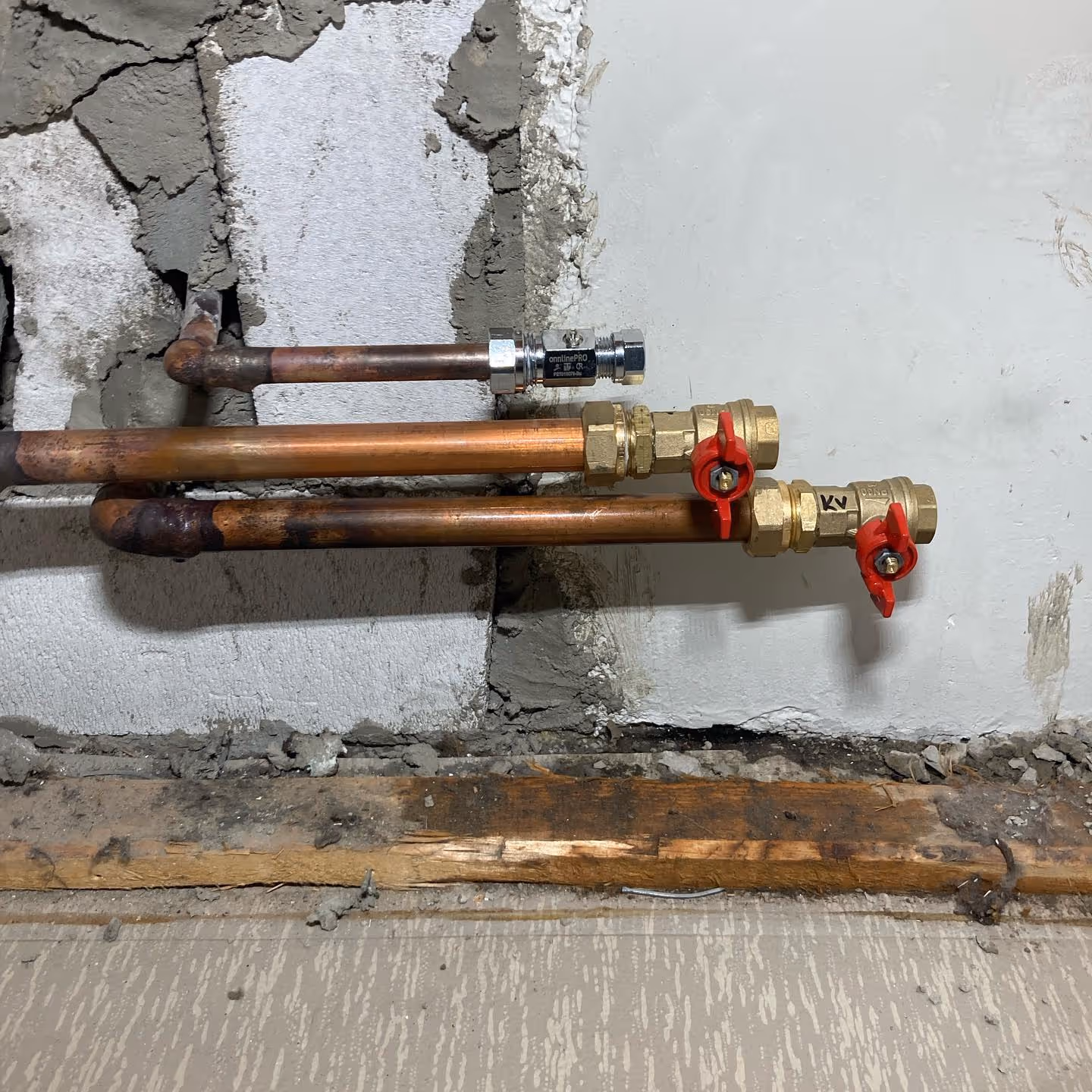 Kupariset putket ja venttiilit on asennettu keskeneräiseen seinään, jossa näkyy rakennusmateriaaleja.