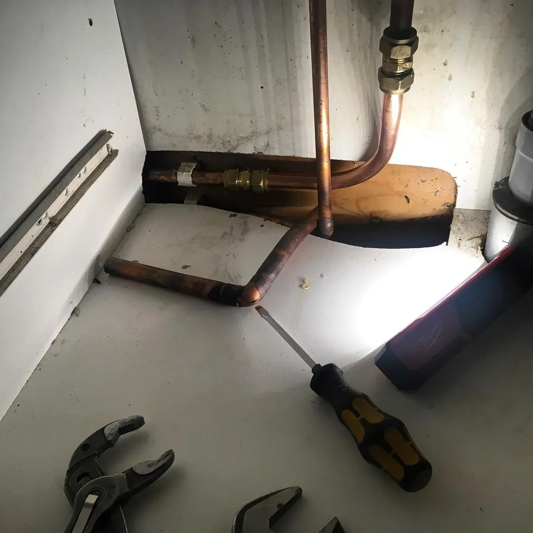 Kupariputket ja putkiliitokset näkyvät ahtaassa tilassa, jossa on myös työkaluja ja taskulamppu.