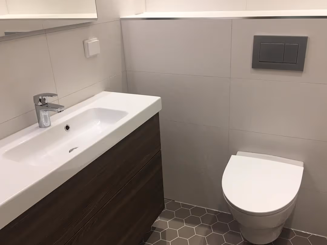 Modernissa kylpyhuoneessa on valkoinen pesuallas tummalla allaskaapilla ja seinään kiinnitetty wc-istuin.