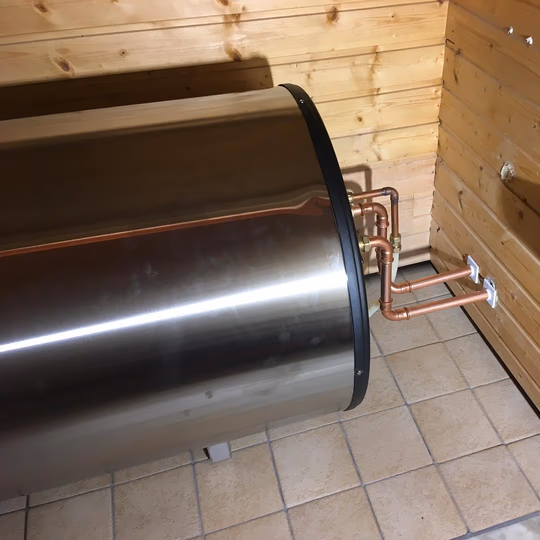 Vaakasuora lämminvesivaraaja, johon on liitetty kuparisia putkia puuseinää vasten laattalattialla.