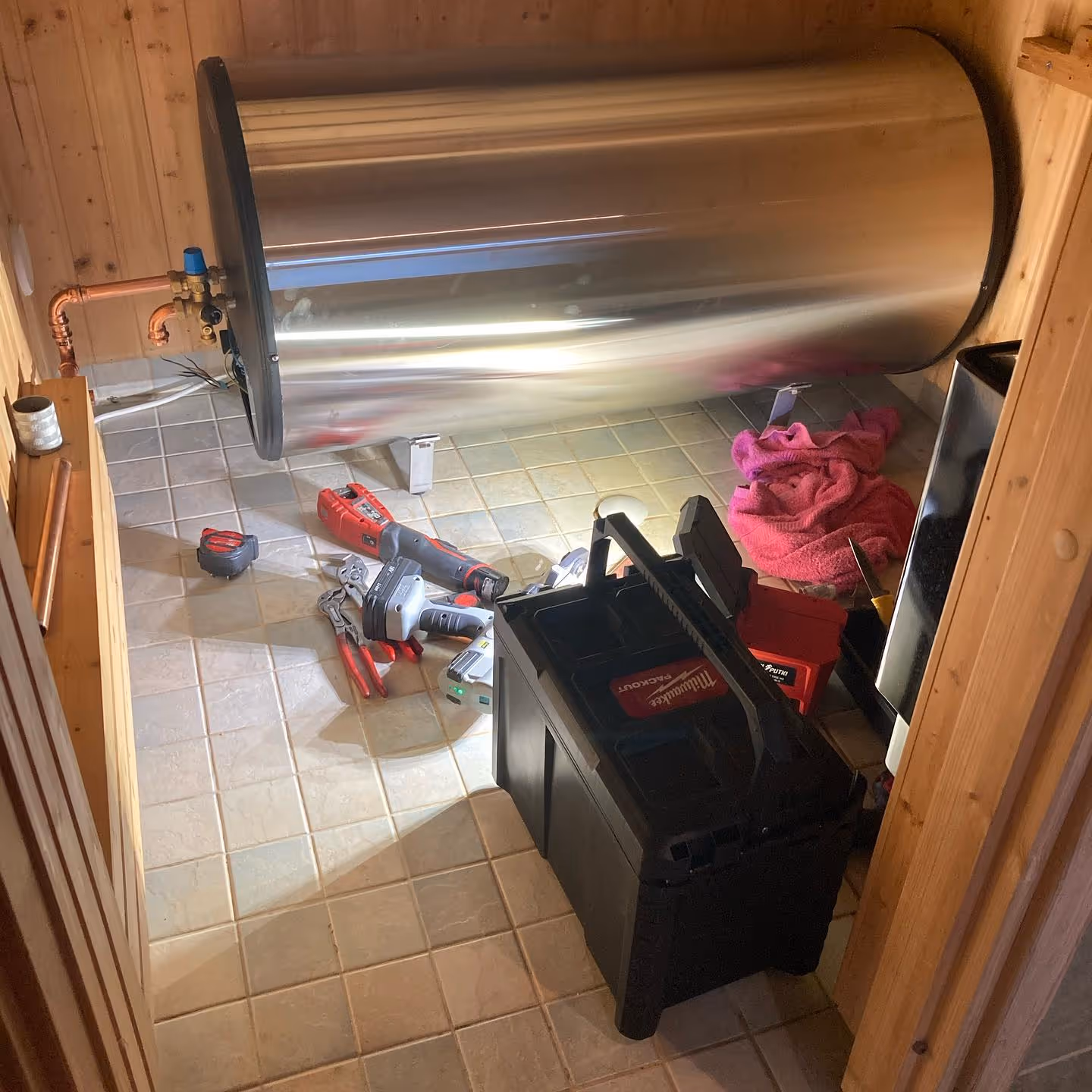 Ruostumattomasta teräksestä valmistettu lämminvesivaraaja, johon on liitetty kupariputkia, on lattialla työkalujen ympäröimänä.