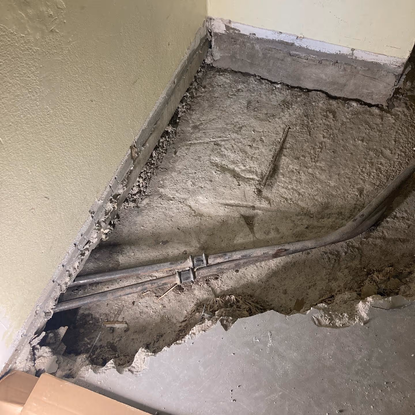 Murtunut betonilattia paljastaa kaksi putkea kulkevan seinän vieressä rakennustyömaalla.