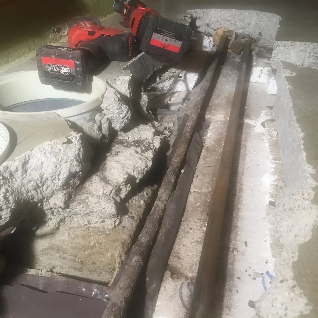 Kaivetussa betonilattiassa näkyy vanhoja, ruosteisia putkia ja rakennustyökaluja.