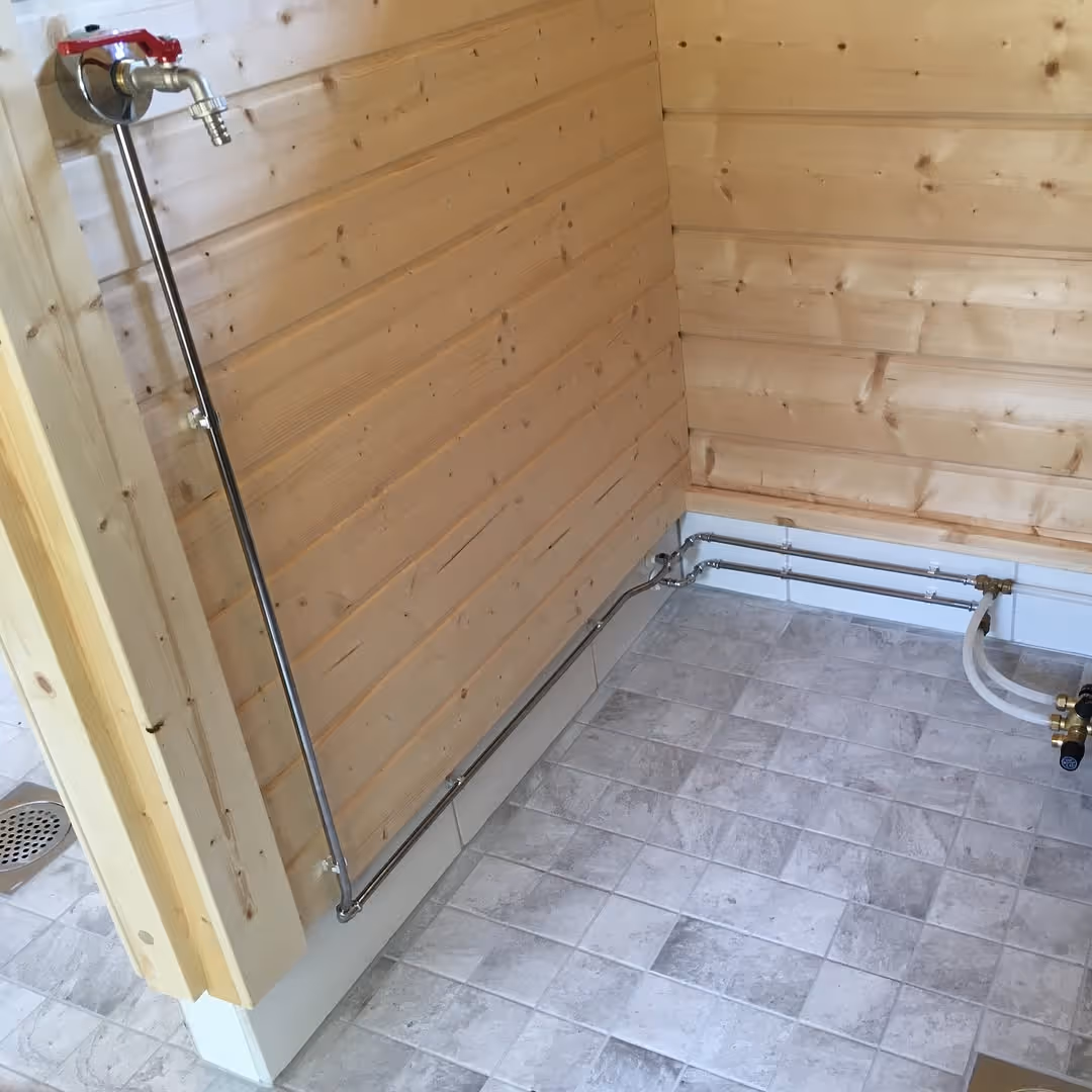 Puuseinäisessä huoneessa näkyy asennettu putkisto hanoineen ja laattalattia.