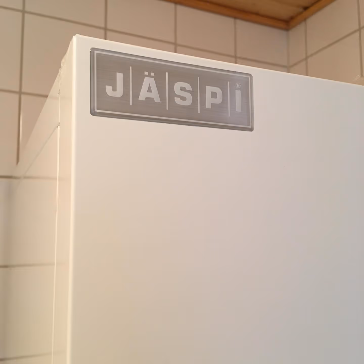Valkoinen lämminvesivaraaja, jossa on harmaa nimikilpi, on sijoitettu laatoitettuun tilaan.